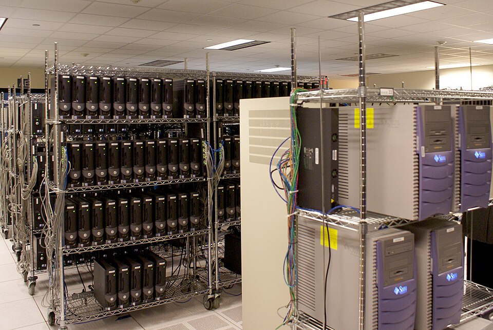 Rows of servers on metal shelving racks in a data centre, with colourful cables running between units