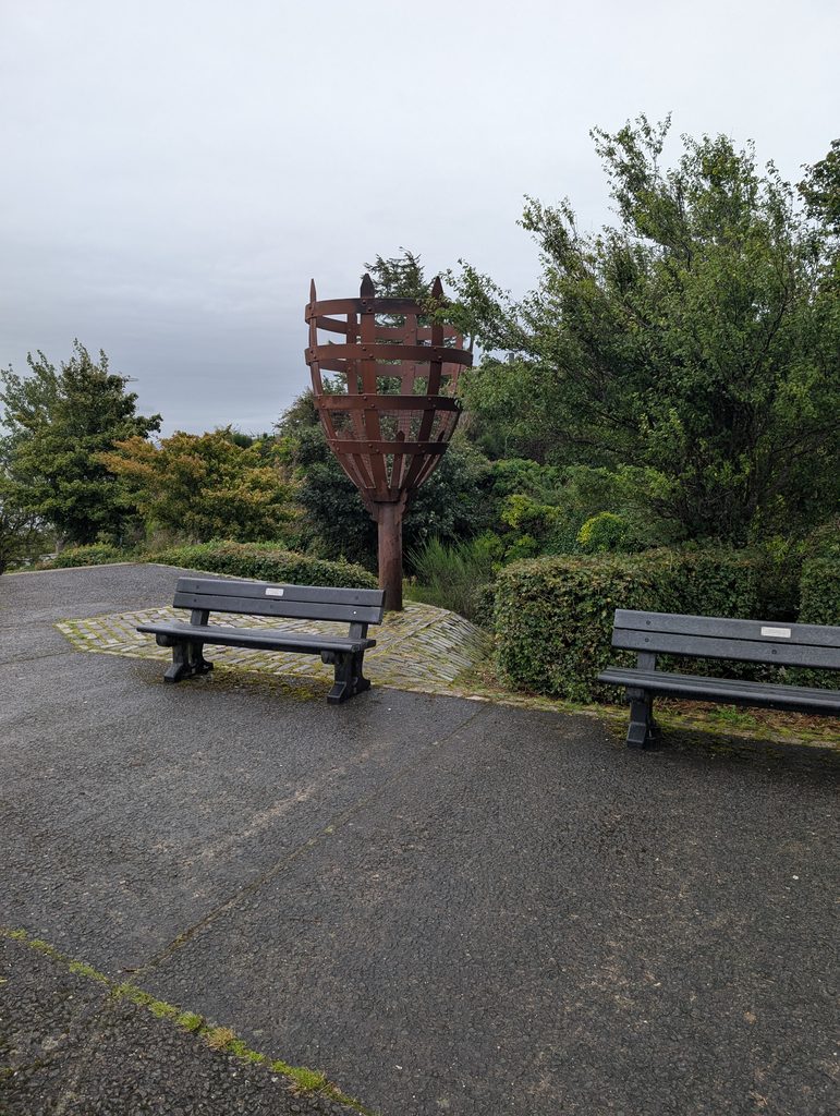 The QEII Jubilee beacon, a metal torch sculpture on Lyle Hill flanked by benches and trees