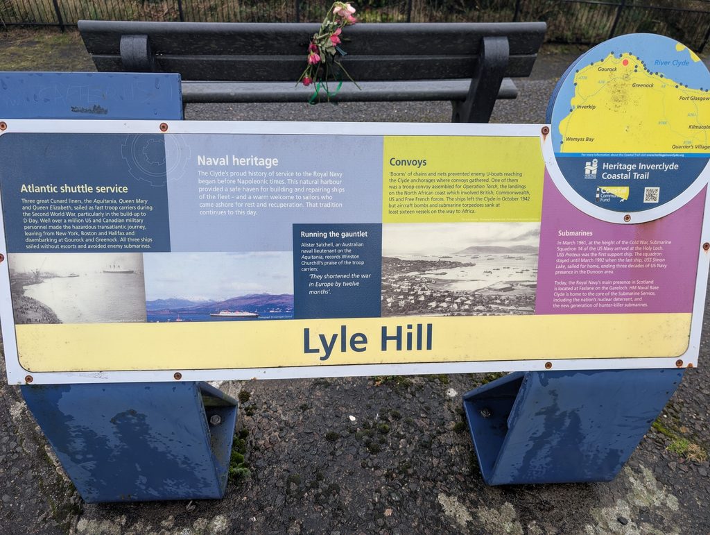 A Lyle Hill heritage information board on naval history, with flowers tied to the bench behind it